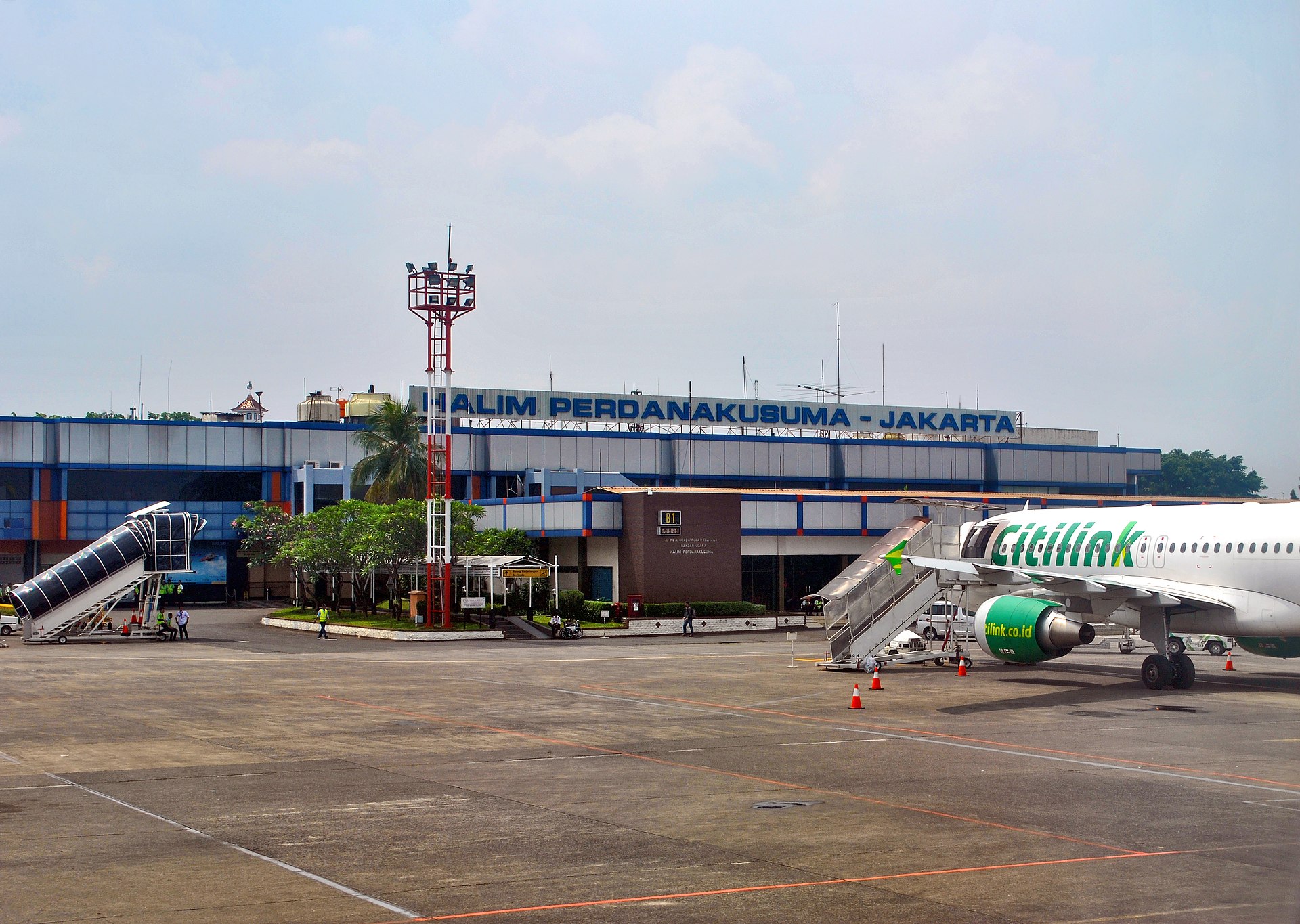 Pesawat penumpang di landasan apron Bandara Halim Perdanakusuma dengan tangga penumpang yang terhubung ke pintu pesawat.